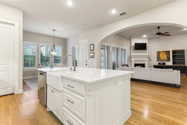 kitchen featuring dishwasher, a sink, a ceiling fan, arched walkways, and light wood-type flooring