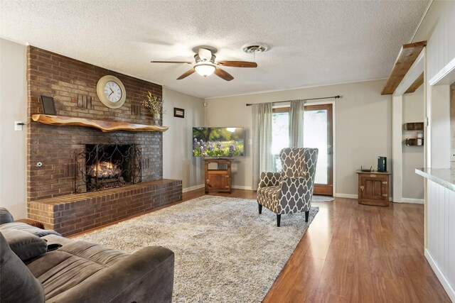 1512 Hulme St, Bowie, TX 76230 - living area with ceiling fan, wood finished floors, a textured ceiling, a brick fireplace, and baseboards