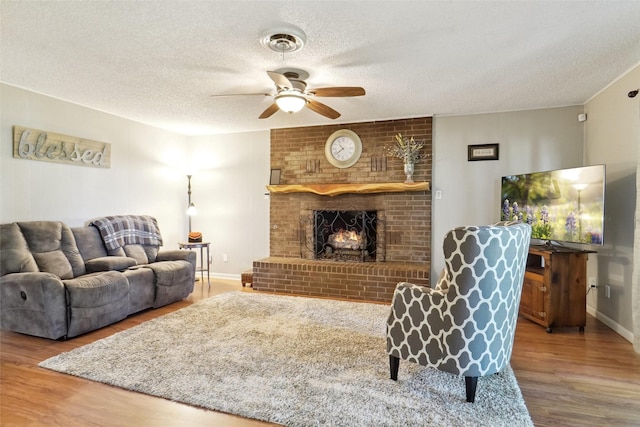 1512 Hulme St, Bowie, TX 76230 - living room with wood finished floors, ceiling fan, a textured ceiling, a fireplace, and baseboards
