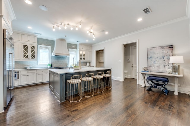 kitchen featuring custom range hood, crown molding, light countertops, backsplash, and white cabinetry
