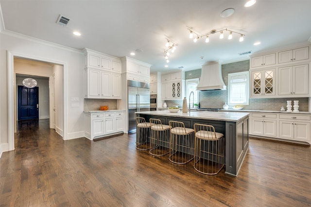 kitchen featuring appliances with stainless steel finishes, custom exhaust hood, light countertops, white cabinets, and backsplash