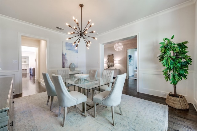 dining room featuring a chandelier, crown molding, wood finished floors, a wainscoted wall, and a decorative wall
