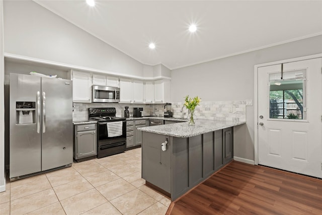 kitchen with appliances with stainless steel finishes, a peninsula, gray cabinets, decorative backsplash, and lofted ceiling