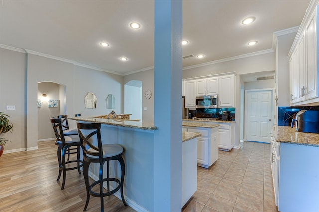 2505 Hillary Trl, Mansfield, TX 76063 - kitchen with stainless steel microwave, arched walkways, white cabinetry, recessed lighting, and a kitchen bar