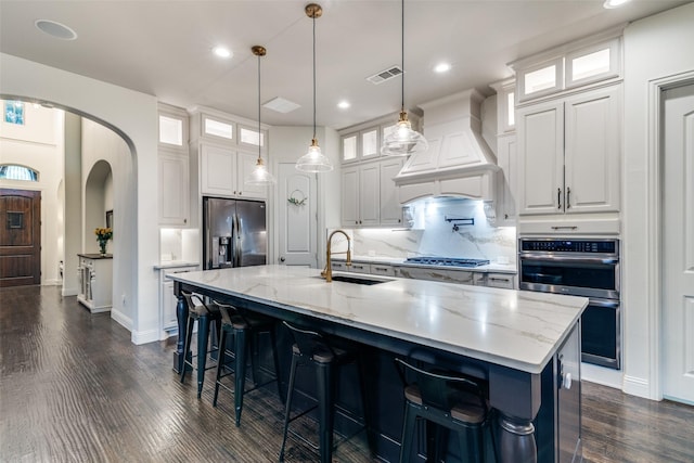 kitchen featuring stainless steel appliances, a sink, custom range hood, dark wood-type flooring, and arched walkways