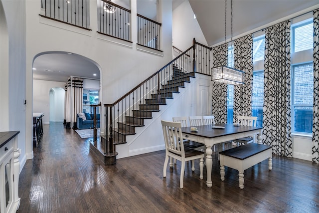 dining space with a high ceiling, arched walkways, baseboards, wood finished floors, and stairway