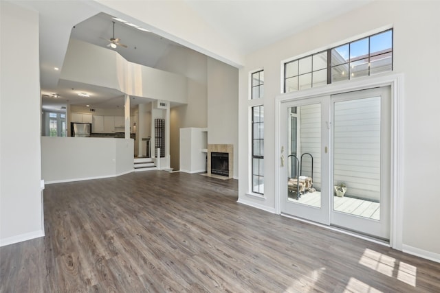 unfurnished living room featuring a tile fireplace, wood finished floors, high vaulted ceiling, a ceiling fan, and baseboards