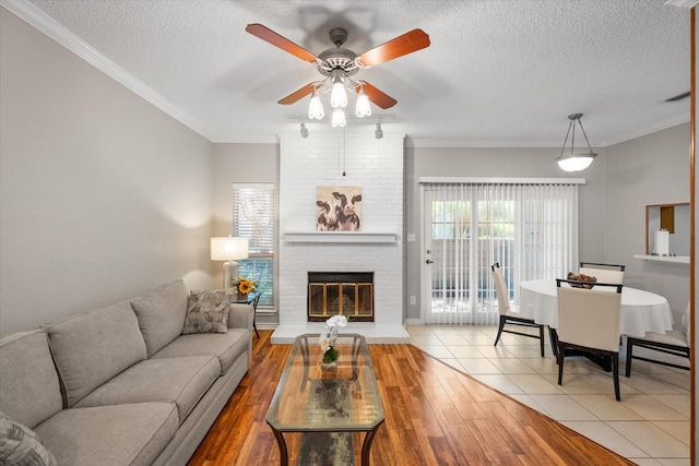 2101 Saint Michaels Dr Unit 109, Arlington, TX 76011 - living room with a textured ceiling, a brick fireplace, ceiling fan, ornamental molding, and light wood finished floors