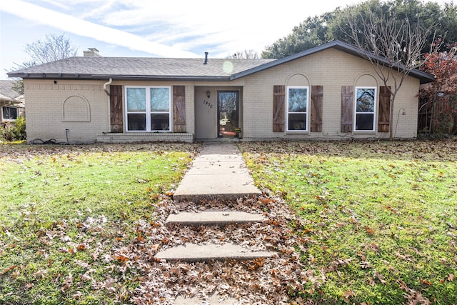 ranch-style home with brick siding, a front yard, roof with shingles, and a chimney