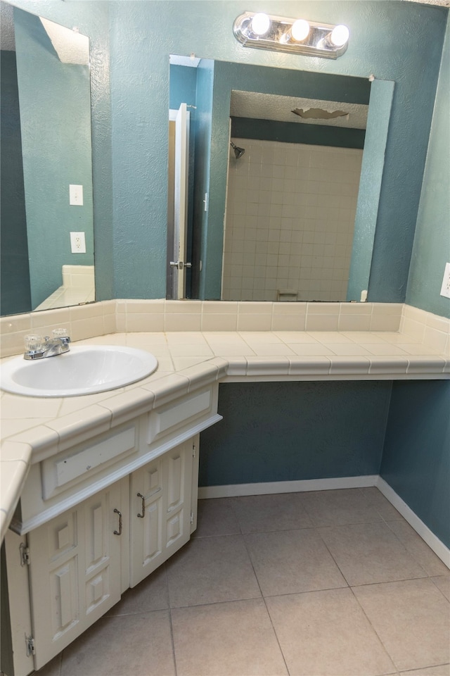 full bath featuring tile patterned floors, a tile shower, and vanity