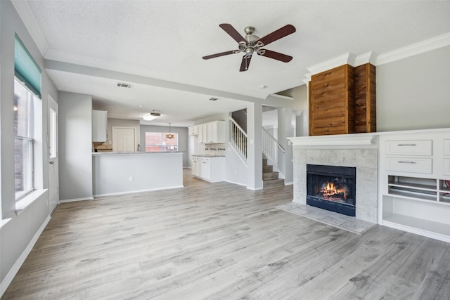 unfurnished living room with ornamental molding, ceiling fan, a tile fireplace, light wood-type flooring, and healthy amount of natural light