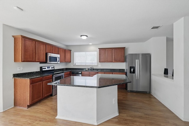 10748 Irish Glen Trl, Fort Worth, TX 76052 - kitchen featuring appliances with stainless steel finishes, a sink, light wood finished floors, a kitchen island, and dark stone countertops