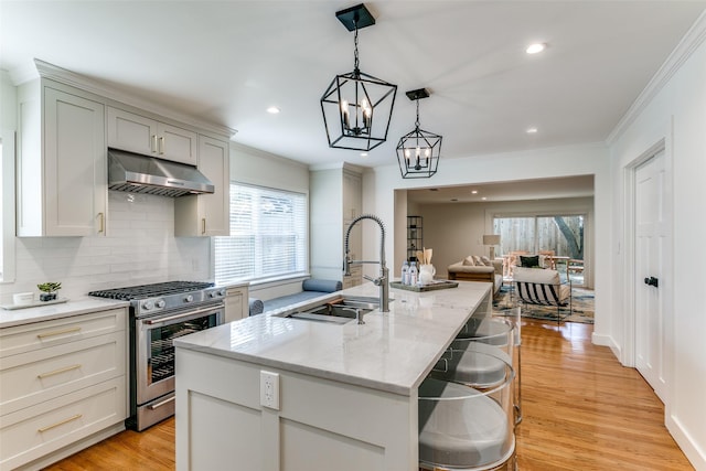 6663 Yosemite Ln, Dallas, TX 75214 - kitchen with stainless steel gas range oven, under cabinet range hood, crown molding, a center island with sink, and tasteful backsplash