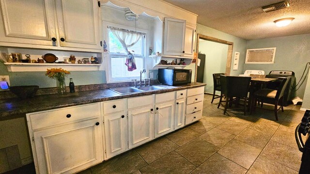 2404 Handley Dr, Fort Worth, TX 76112 - kitchen featuring black microwave, a sink, a textured ceiling, dark countertops, and white cabinetry