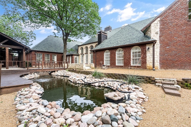 1201 Tralee Ln, Garland, TX 75044 - back of house with roof with shingles, a small pond, a deck, brick siding, and a chimney