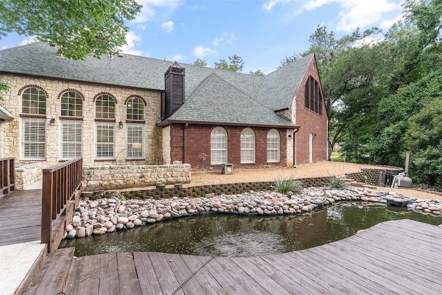 1201 Tralee Ln, Garland, TX 75044 - rear view of house with a shingled roof, stone siding, and a chimney