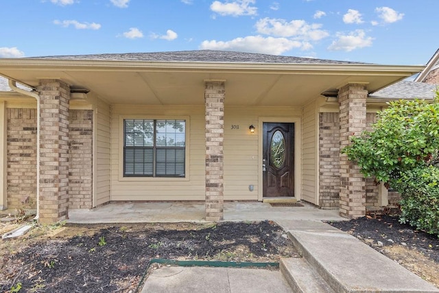 doorway to property featuring a shingled roof and brick siding