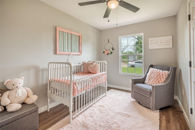 bedroom featuring wood finished floors, baseboards, a crib, and ceiling fan
