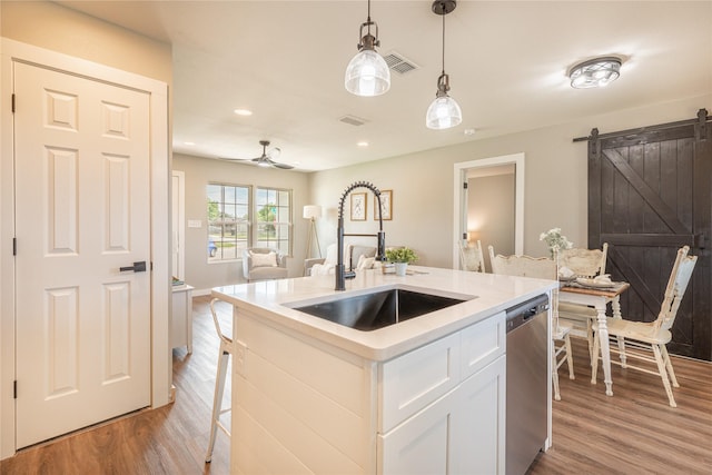 kitchen with a sink, dishwasher, light wood finished floors, a barn door, and recessed lighting