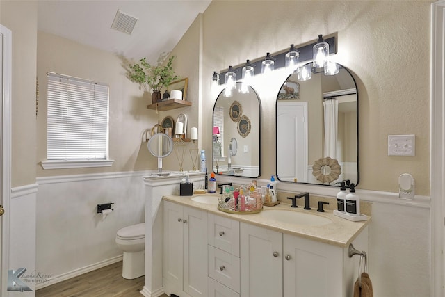 5249 Western Plains Ave, Abilene, TX 79606 - bathroom with a wainscoted wall, wood finished floors, toilet, double vanity, and vaulted ceiling