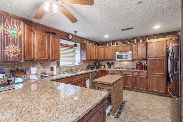 5295 Ganzer Rd W, Krum, TX 76249 - kitchen with appliances with stainless steel finishes, a sink, a textured ceiling, brown cabinets, and a ceiling fan