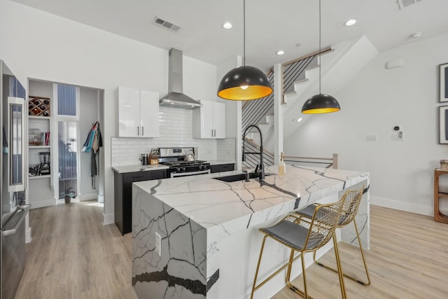 2102 N Prairie Ave Unit 105, Dallas, TX 75204 - kitchen with appliances with stainless steel finishes, a sink, wall chimney range hood, white cabinetry, and light wood-style flooring
