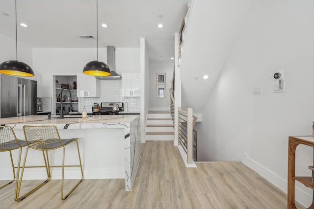 2102 N Prairie Ave Unit 105, Dallas, TX 75204 - kitchen with wall chimney exhaust hood, light wood-style floors, white cabinetry, appliances with stainless steel finishes, and light stone counters