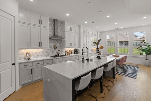 507 Melody Meadow Dr, Rockwall, TX 75087 - kitchen with wall chimney exhaust hood, light wood-style floors, a center island with sink, gas stovetop, and decorative backsplash