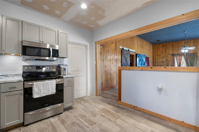 442 W Mccart St, Krum, TX 76249 - kitchen featuring appliances with stainless steel finishes, gray cabinetry, wood walls, light stone countertops, and ceiling fan