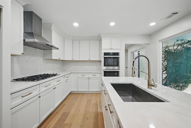6407 Laurel Valley Rd, Dallas, TX 75248 - kitchen with wall chimney range hood, stainless steel appliances, a sink, light wood-type flooring, and backsplash