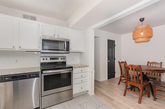 8750 Park Ln Unit 151, Dallas, TX 75231 - kitchen featuring appliances with stainless steel finishes, tasteful backsplash, light stone countertops, white cabinetry, and hanging light fixtures