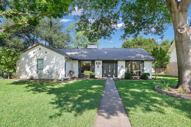 ranch-style home with a chimney, a front yard, and a shingled roof
