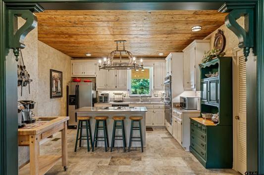 1847 N State Highway 19, Emory, TX 75440 - kitchen featuring appliances with stainless steel finishes, white cabinetry, a chandelier, wooden ceiling, and a kitchen bar