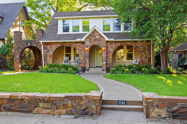 1143 N Winnetka Ave, Dallas, TX 75208 - english style home featuring stone siding, covered porch, a shingled roof, and a front lawn