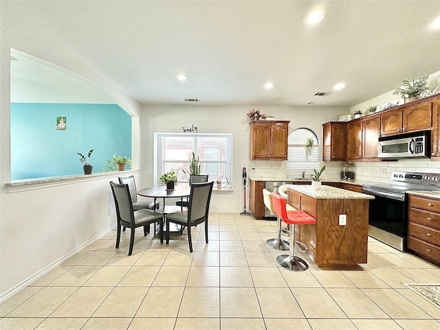 6468 Payton Dr, Fort Worth, TX 76131 - kitchen with stainless steel appliances, a center island, backsplash, light tile patterned floors, and a kitchen bar