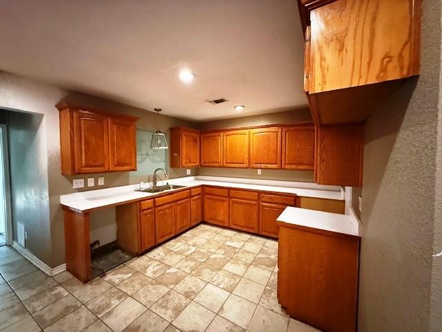 426 Gun Club Rd, Denison, TX 75021 - kitchen featuring a sink, brown cabinets, light countertops, decorative light fixtures, and light tile patterned floors