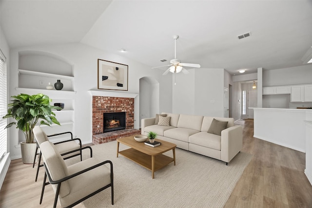2402 Greenfield Cir, Garland, TX 75040 - living room featuring built in features, light wood-style flooring, ceiling fan, a brick fireplace, and lofted ceiling