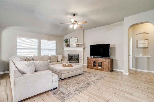 living area featuring a ceiling fan, wood finished floors, arched walkways, a fireplace, and baseboards