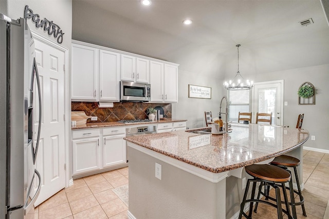 kitchen with stainless steel appliances, a sink, light tile patterned flooring, backsplash, and vaulted ceiling