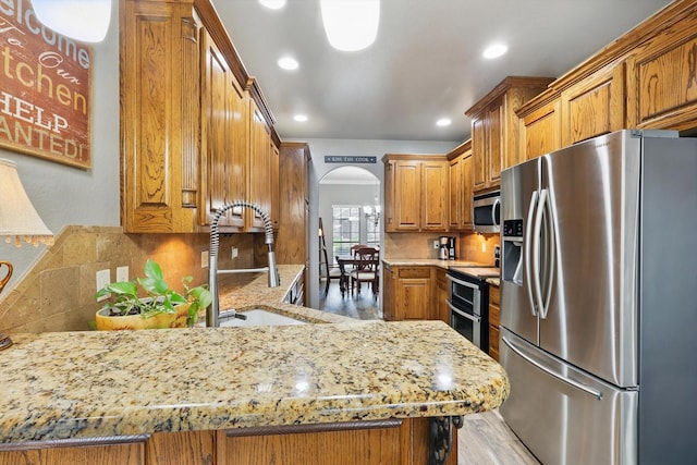 2210 Ridgewood Dr, Bridgeport, TX 76426 - kitchen with stainless steel appliances, a sink, arched walkways, brown cabinets, and decorative backsplash