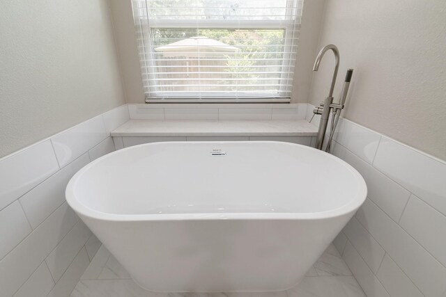 7300 Frances Ct, North Richland Hills, TX 76182 - bathroom featuring tile walls, a soaking tub, marble look tiles, and a wainscoted wall