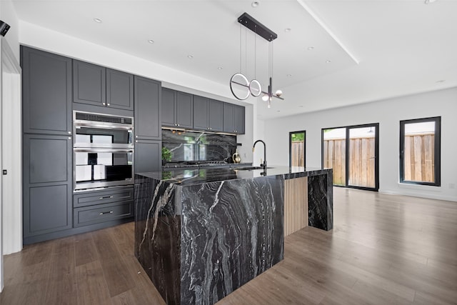 2535 Exline St, Dallas, TX 75215 - kitchen with a sink, dark stone counters, stainless steel double oven, dark wood-type flooring, and a center island with sink