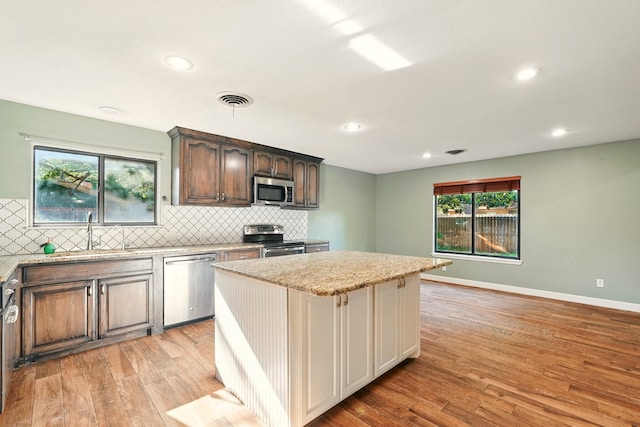 kitchen with appliances with stainless steel finishes, a sink, light wood finished floors, a kitchen island, and tasteful backsplash