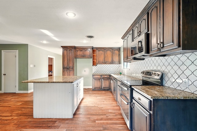 kitchen featuring stainless steel appliances, decorative backsplash, a sink, light wood-type flooring, and dark stone counters