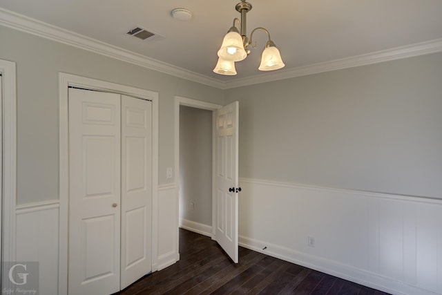 unfurnished bedroom featuring a chandelier, dark wood-style flooring, ornamental molding, a closet, and baseboards