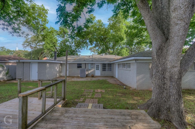 rear view of house with brick siding, a deck, a lawn, central AC, and a patio
