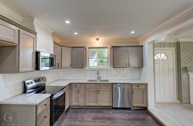 kitchen with appliances with stainless steel finishes, a sink, crown molding, dark wood-style flooring, and light stone countertops