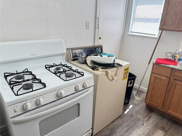 2414 Marfa Ave, Dallas, TX 75216 - kitchen with white gas range, washer / dryer, brown cabinetry, light wood finished floors, and a textured wall