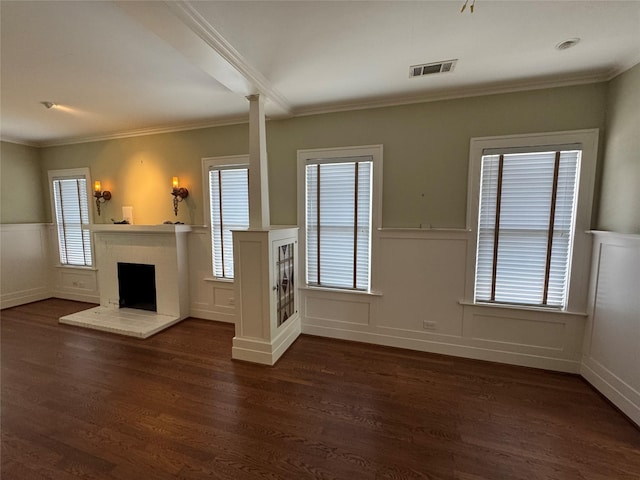 unfurnished living room featuring crown molding, dark wood-style floors, a wainscoted wall, decorative columns, and a brick fireplace
