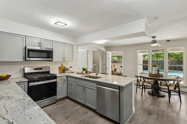 6908 Heatherknoll Dr, Dallas, TX 75248 - kitchen with stainless steel appliances, gray cabinetry, a sink, a peninsula, and tasteful backsplash